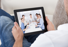 Businessman on a video call chatting to colleagues in a meeting visible on the screen of his tablet